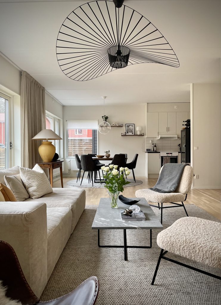 Ljust vardagsrum med beige soffa, svart pandellampa och öppen planlösning